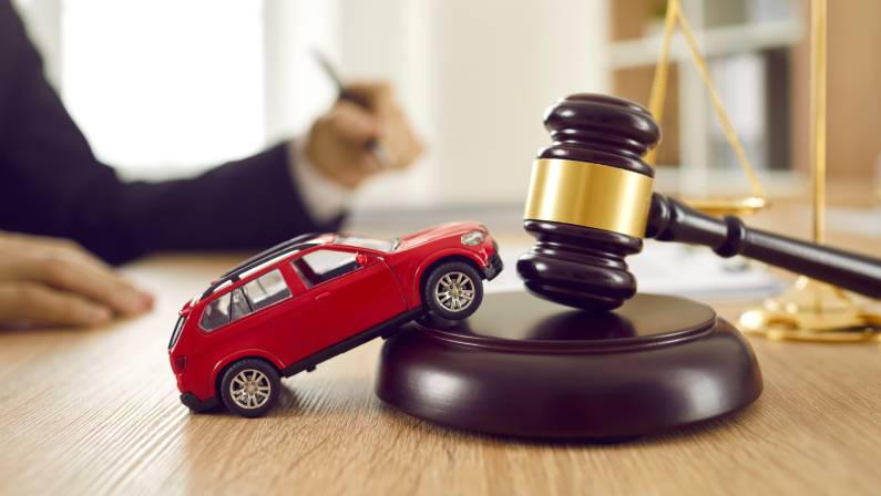 Small car model on wooden desk with judge's hammer.