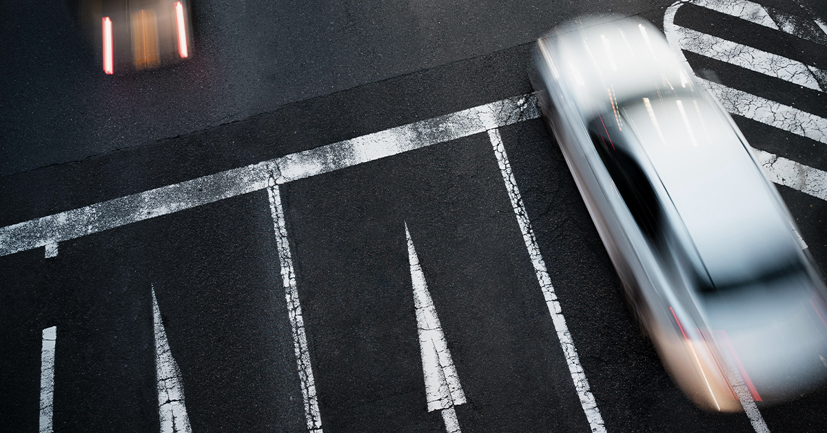 High-angle motion blur of a silver car speeding on asphalt.
