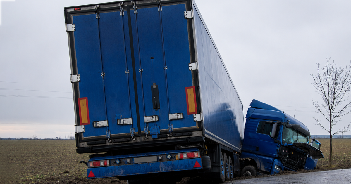 Blue semi-truck crashed off a wet road into a muddy field.