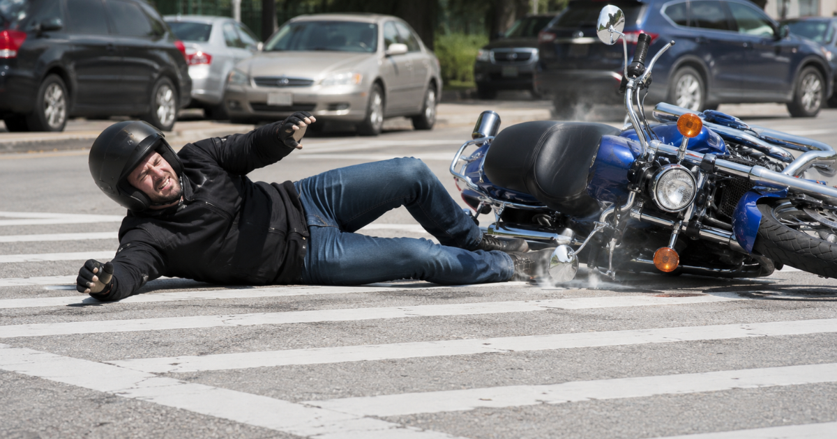 Injured biker lying on a crosswalk beside a fallen blue motorcycle after a crash.