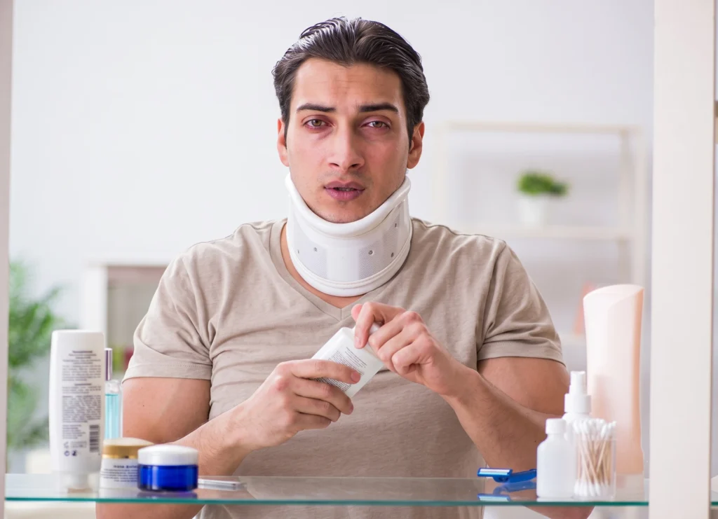 Injured man in a neck brace holding a medicine bottle in front of a mirror.