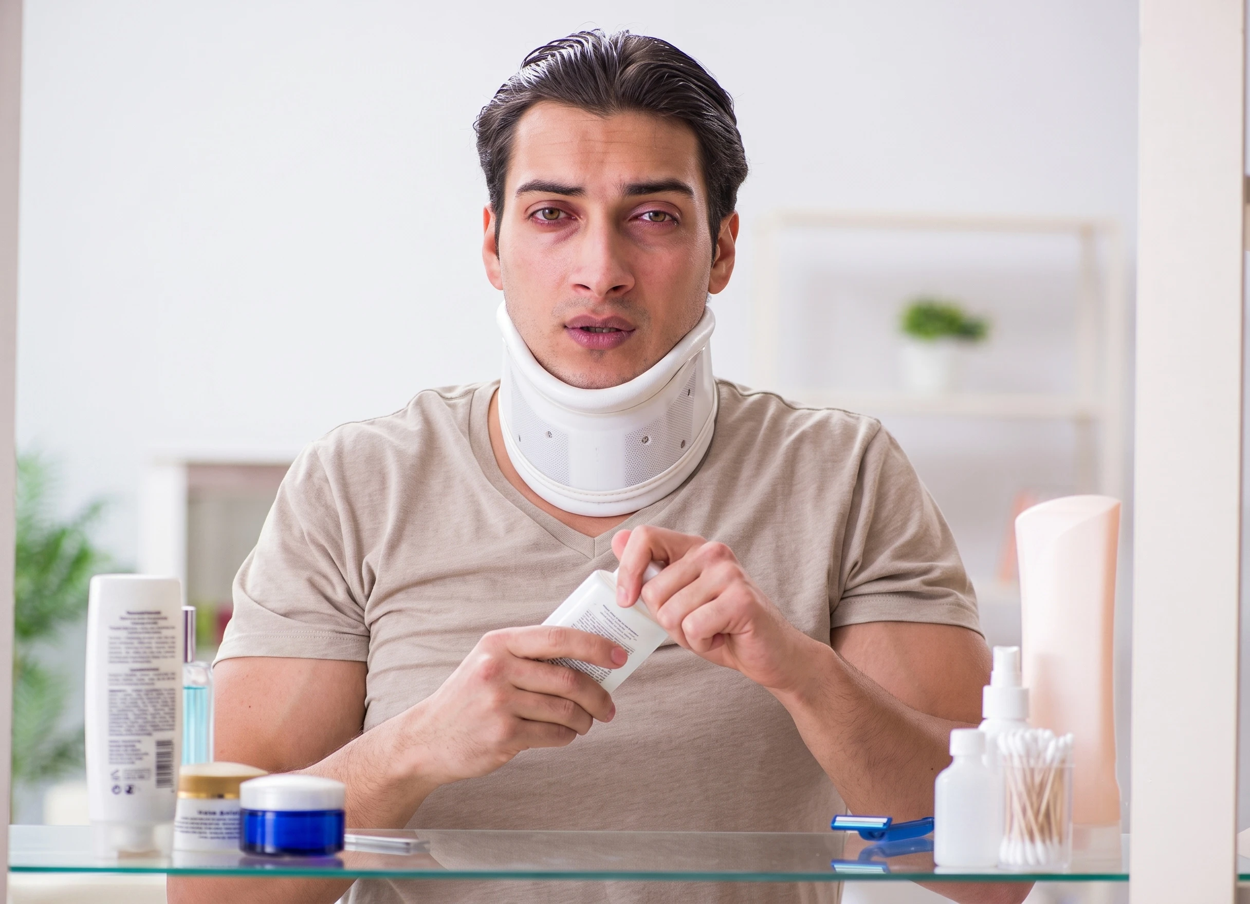 Injured man in a neck brace holding a medicine bottle in front of a mirror.