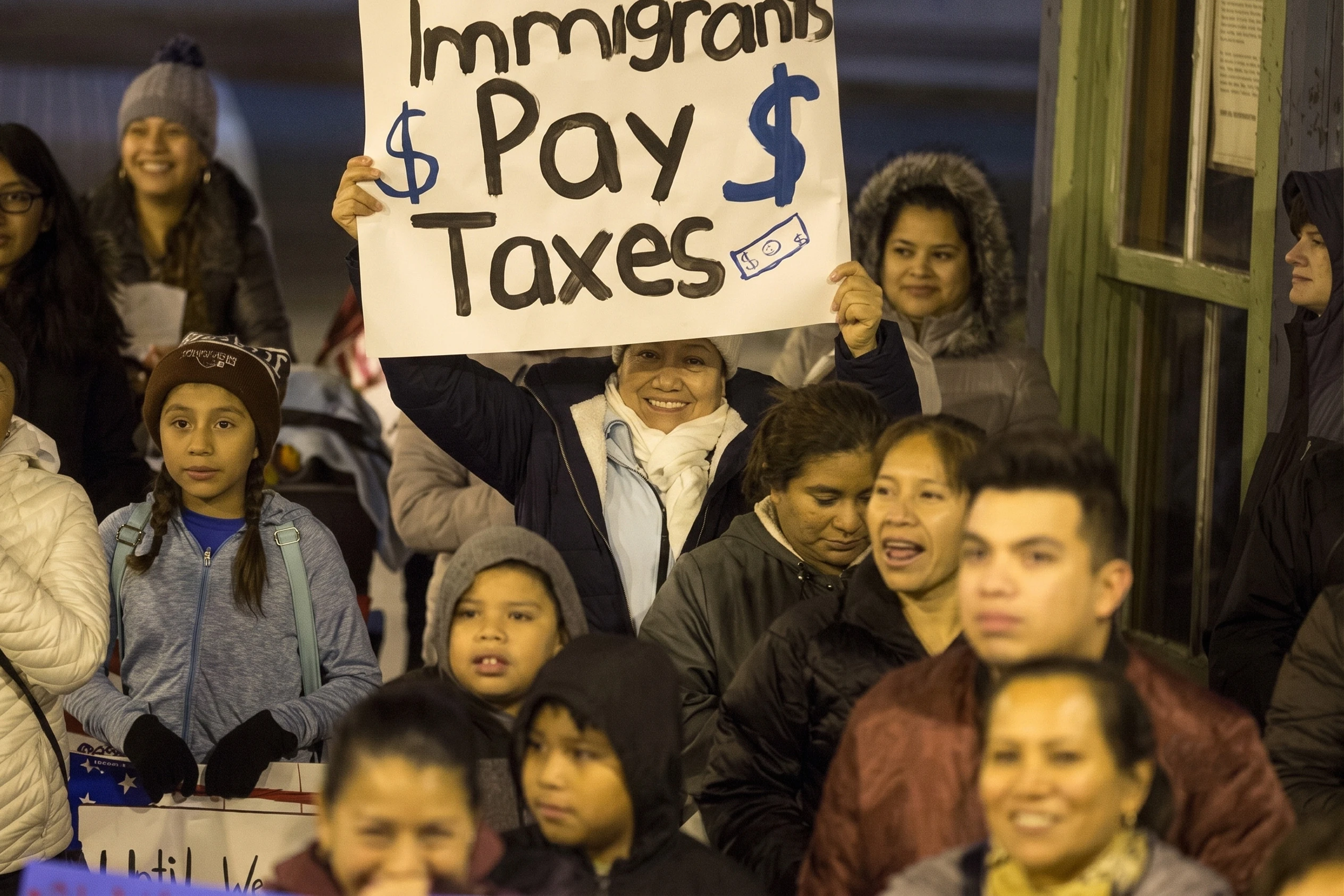 Woman holding a sign reading "Immigrants Pay Taxes" at a rally.