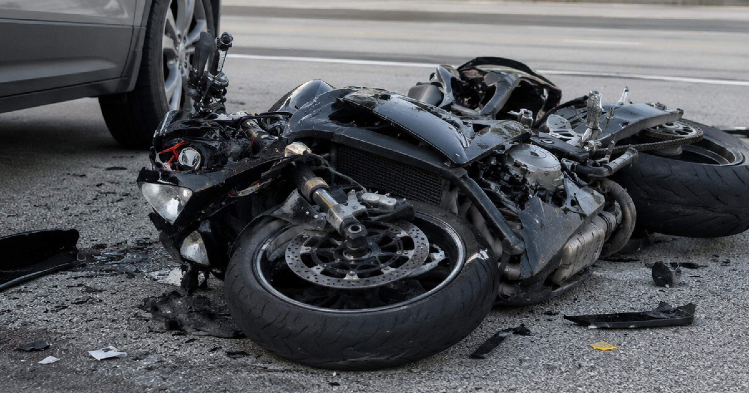 Damaged motorcycle lying on a city street beside a car after a crash.