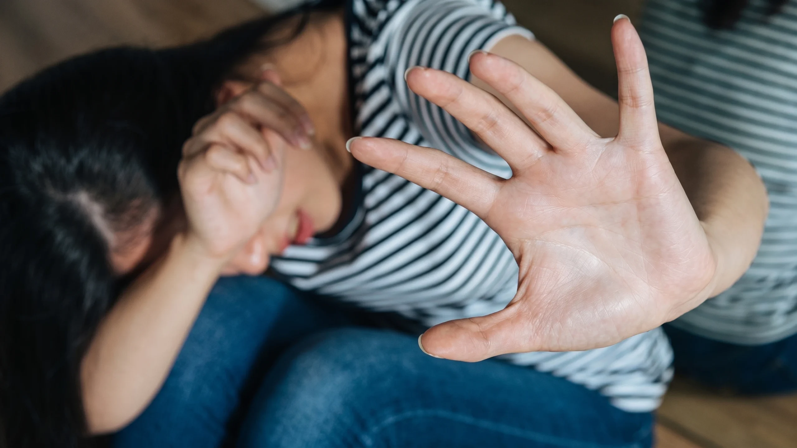 Close-up of a distressed woman holding out her open hand to signal "stop" or self-defense while covering her eyes, depicting domestic violence or abuse awareness.