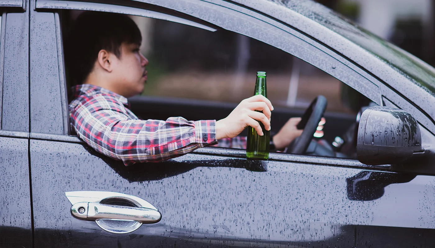 Man holding beer bottle while sitting inside a parked car