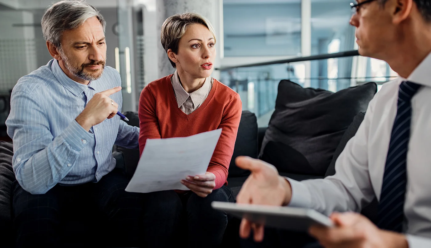 Couple discussing paper documents intently during meeting with financial advisor.