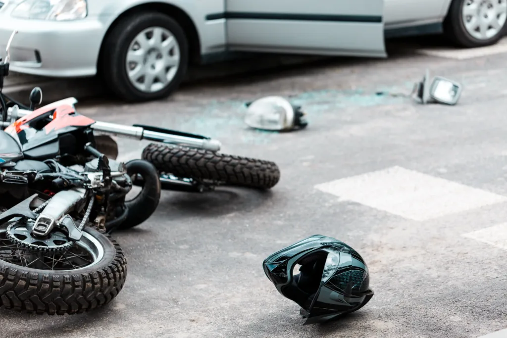 A crashed motorcycle lying on the street next to a helmet and scattered broken glass.