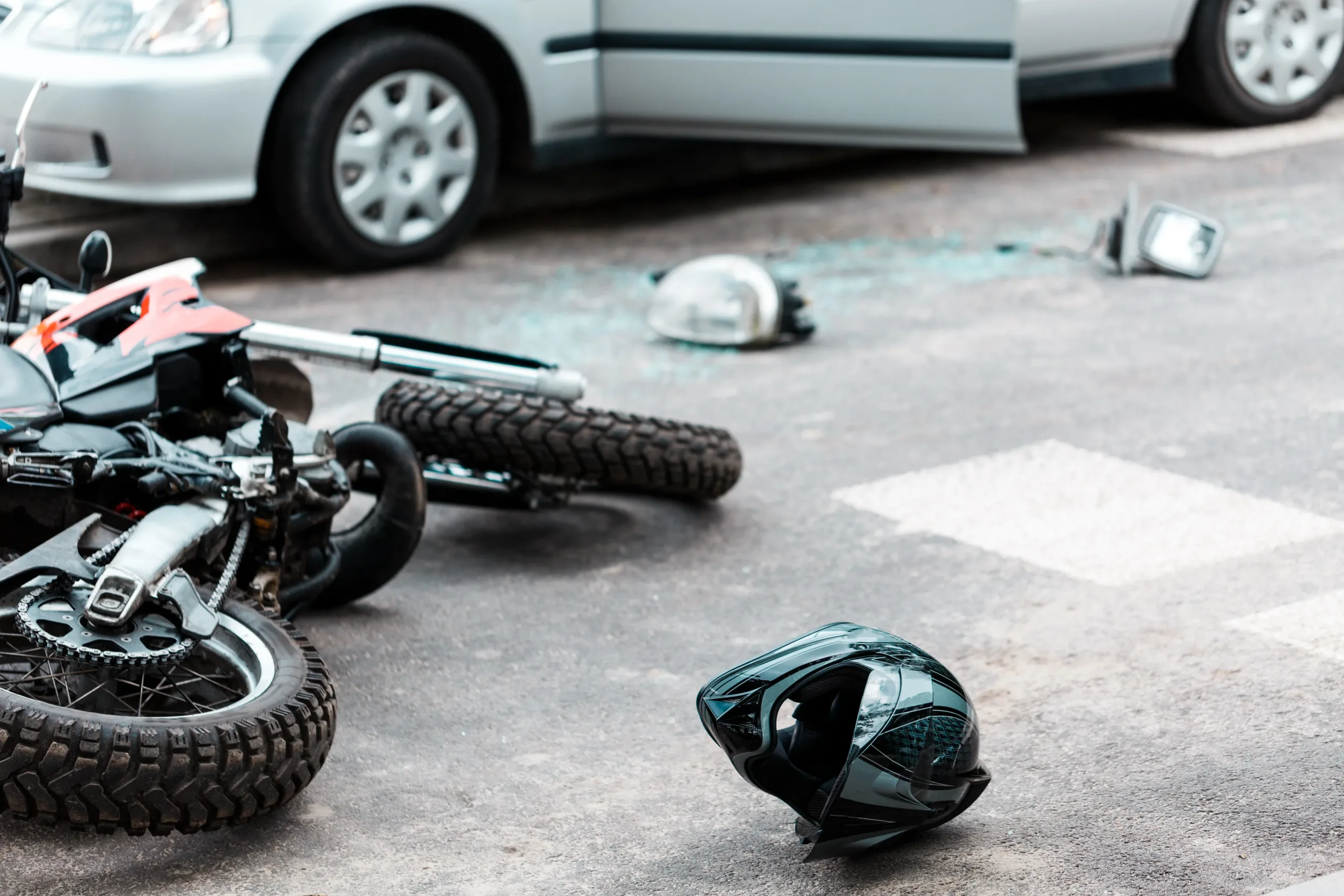 A crashed motorcycle lying on the street next to a helmet and scattered broken glass.