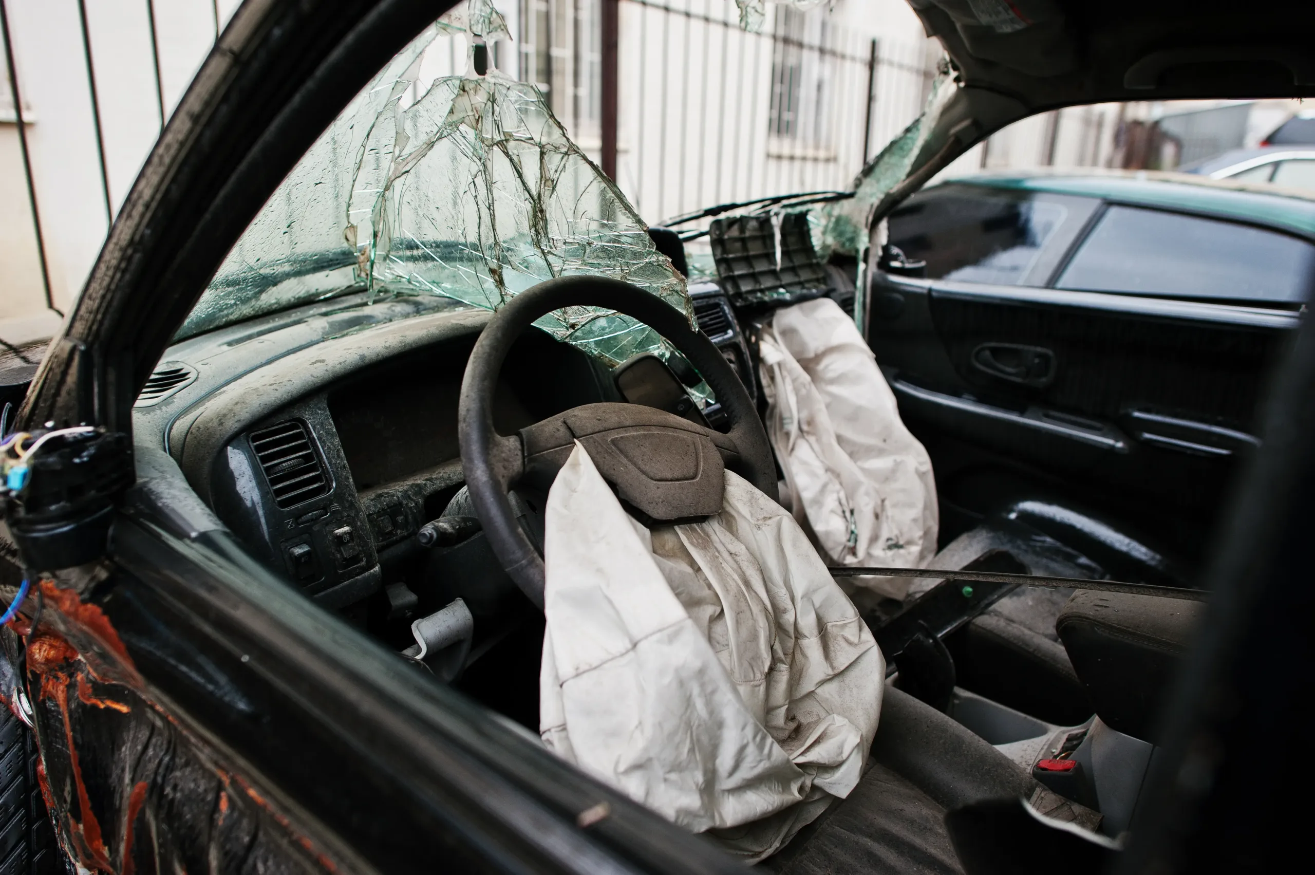 Interior view of a severely damaged car with deployed airbags and a shattered windshield.